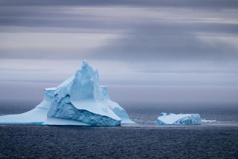 Two icebergs floating in the ocean under a cloudy sky.