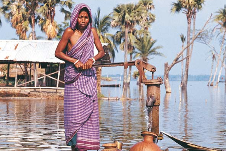 A woman in a sari standing next to a water pump.