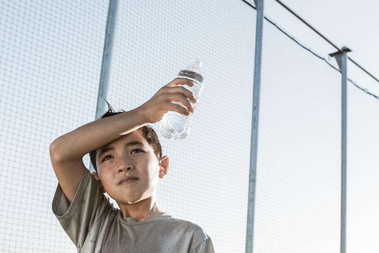 A boy is holding a water bottle in front of a fence.
