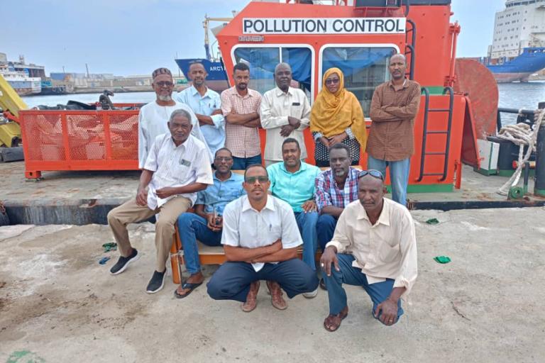 Group of people posing for a photo in front of a vessel marked with "pollution control.