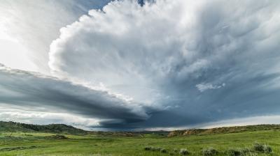 A large storm cloud is seen over a grassy field.
