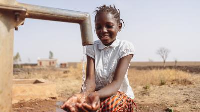 A young girl is standing next to a water pump.