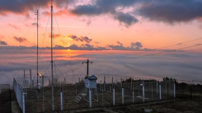 A radio station on top of a hill with clouds in the background.