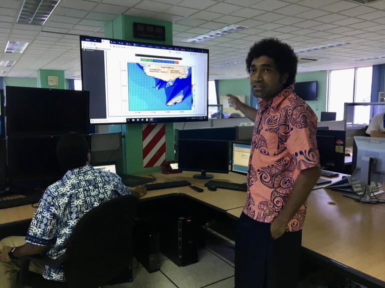 A man in a hawaiian shirt standing in front of two monitors.