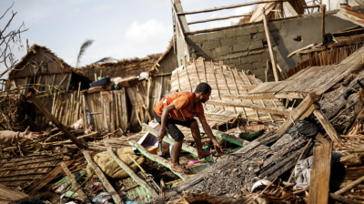 A person salvaging materials amidst the ruins of destroyed buildings.